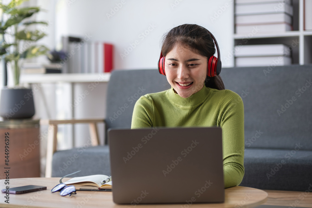 Young Woman Sitting and Working in the Living Room with Laptop and Headphones, Modern Home Office Setup, Remote Work, Productivity, and Comfort in a Cozy Living Space Young Woman Sitting and Working in the Living Room with Laptop and Headphones, Modern Home Office Setup, Remote Work, Productivity, and Comfort in a Cozy Living Space