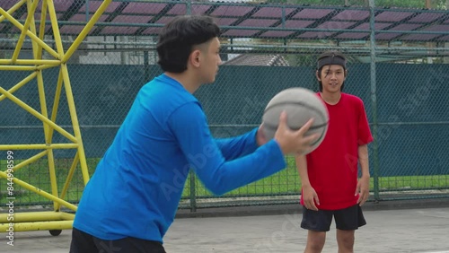 Group Of Young Asian Men Practicing Basketball By Bouncing The Ball At An Outdoor Court