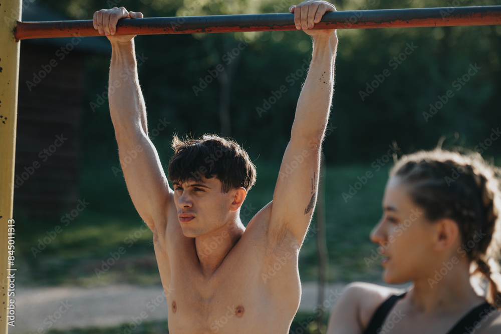 Naklejka premium Young man performing an outdoor exercise on a pull-up bar, emphasizing fitness and determination in a natural setting.