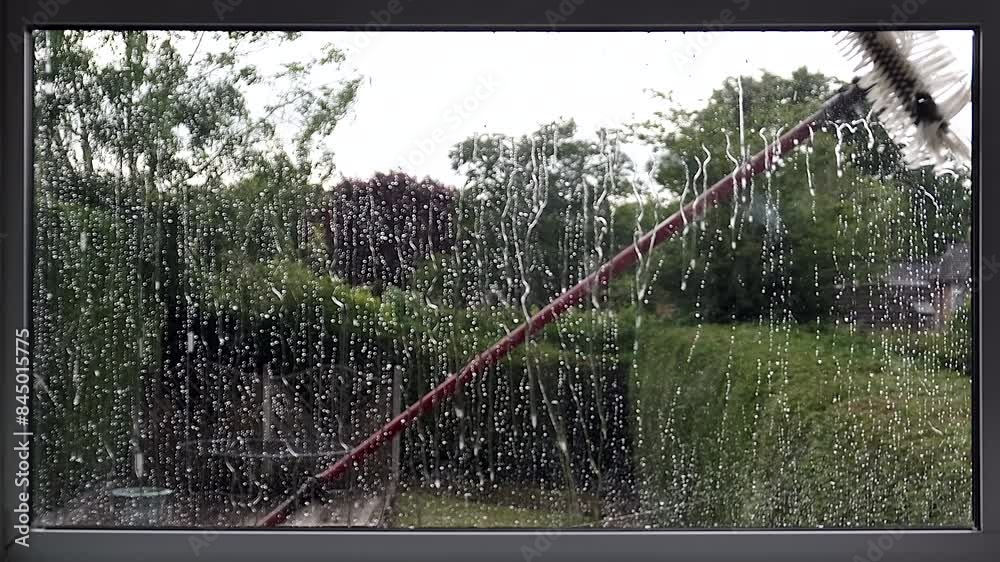A window cleaners brush on a long pole being use to spray water to clean an exterior window on the first floor of a house.