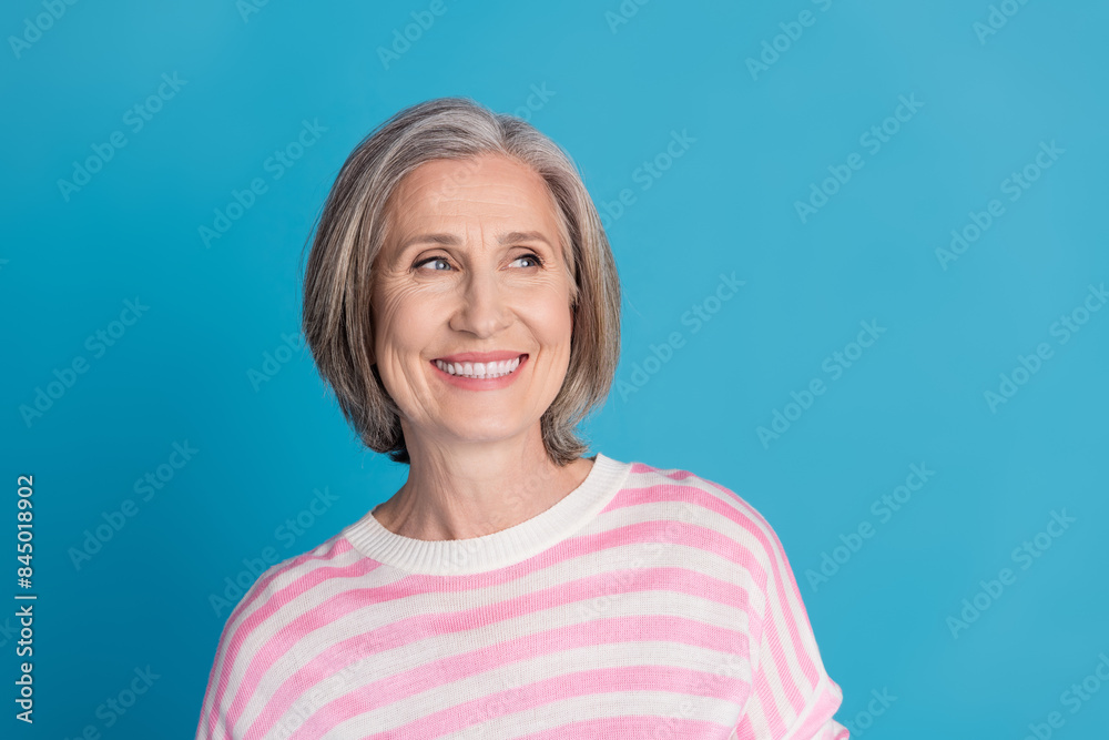 Photo portrait of nice senior woman look empty space wear trendy striped outfit isolated on blue color background Photo portrait of nice senior woman look empty space wear trendy striped outfit isolated on blue color background