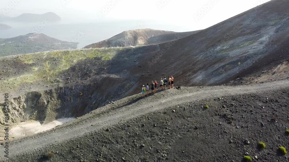 Aerial view of tourists watching the ash-covered slope of a volcano crater on the island of Vulcano near Sicily during the day. Aerial view of tourists watching the ash-covered slope of a volcano crater on the island of Vulcano near Sicily during the day.