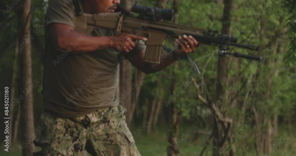 Designated marksman hidden in the forest, aiming a FN Herstal SCAR 17 rifle.