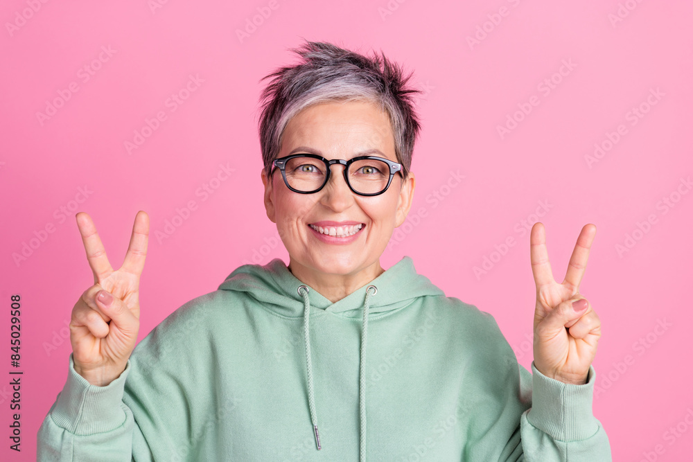 Photo of cheerful cool lady dressed khaki sweatshirt showing two v-signs empty space isolated pink color background