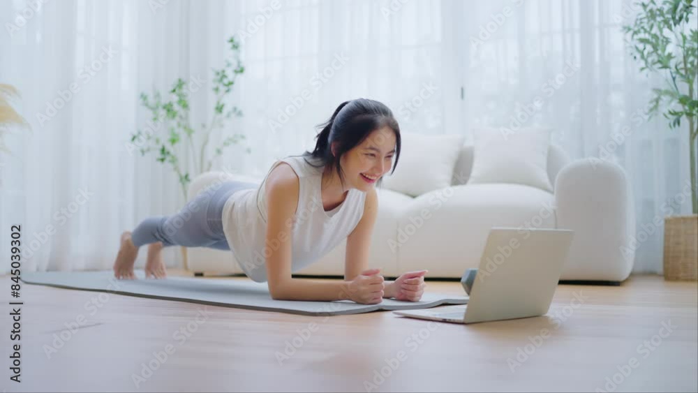 Young Asian woman in sportswear doing plank on training mat while watching online workout tutorials on laptop in the living room. Sport and recreation concept Young Asian woman in sportswear doing plank on training mat while watching online workout tutorials on laptop in the living room. Sport and recreation concept