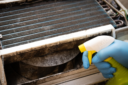 Latex gloved hand applying spray to kill black mold and clean window air conditioning unit.
