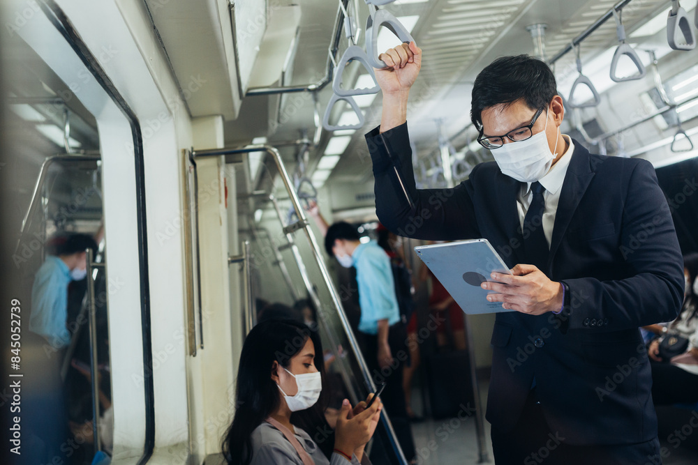 Asian business man wearing protective face mask wathching on digital tablet, Hand holding on a handrail in public subway travel to work Asian business man wearing protective face mask wathching on digital tablet, Hand holding on a handrail in public subway travel to work