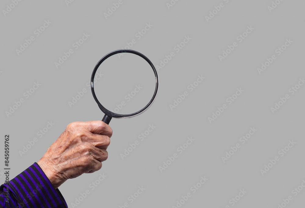 Close-up of an old woman's hand holding a magnifying glass against a gray background.