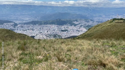 Ascending panoramic view of the city of Quito- Ecuador from Cruz Loma, with the feet of a person sitting on the grass in the foreground.