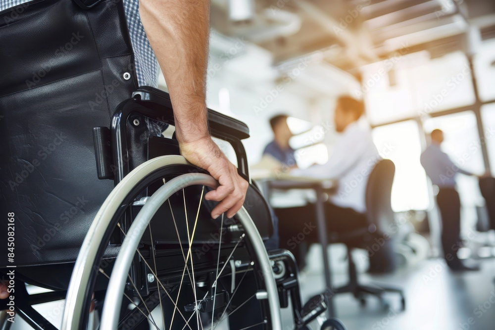 A business man in a wheelchair sits in a large room with a potted plant in the background