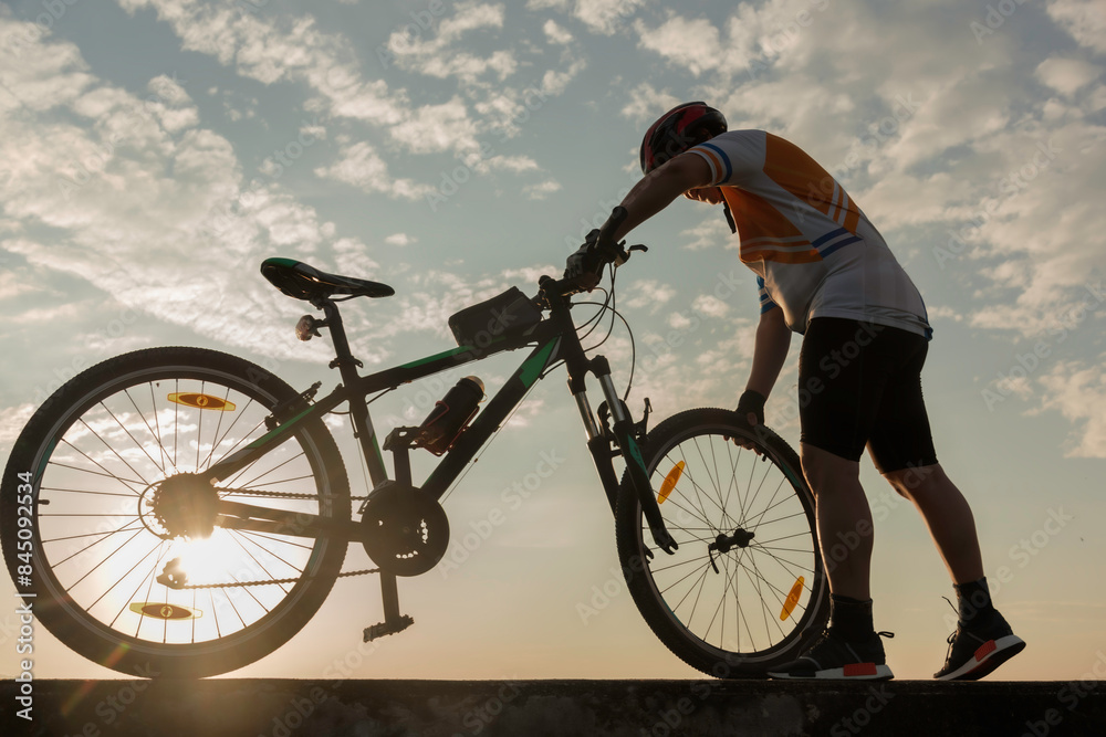 Fototapeta premium Man cyclist repairing a bike against the background of sky