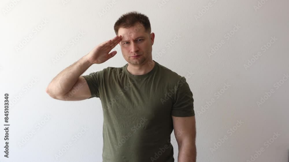 A man in a military hacky sack t-shirt salutes with his hand. A man in a military hacky sack t-shirt salutes with his hand.