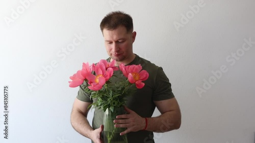 A man in a hacky t-shirt holds a vase of peonies and points to the camera photo