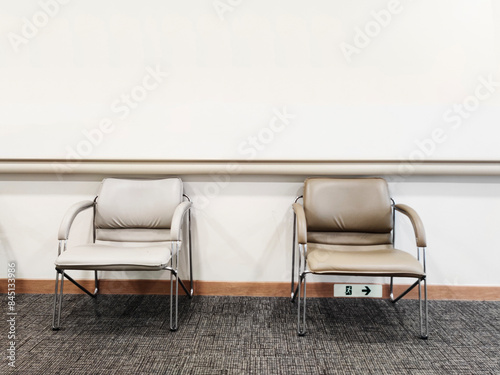 Two sleek, modern chairs with metal legs and cushioned seats sit side by side in a minimalist waiting room with a plain and simplistic light grey wall, exuding a calm, chic and stylish vibe.