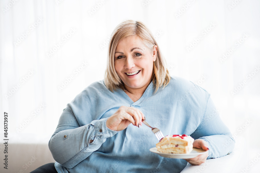 Portrait of beautiful young overweight woman at home, eating slice of cake, enjoying sweet taste. Portrait of beautiful young overweight woman at home, eating slice of cake, enjoying sweet taste.