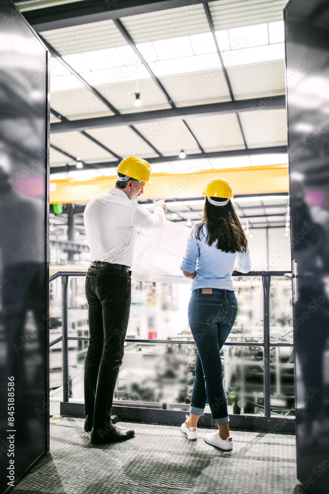 Two project managers standing in modern industrial factory. Manufacturing facility with robotics, robotic arms and automation. Storing products and materials in warehouse. Two project managers standing in modern industrial factory. Manufacturing facility with robotics, robotic arms and automation. Storing products and materials in warehouse.