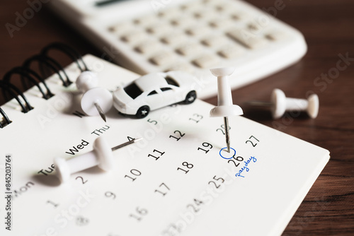 For payment plan, schedule, buy or sell property planning concept. Close up of embroidered white pins on calendar on the 26th with hand writing payday ,blurred calculator and miniature car