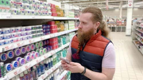 Man manager merchandiser control the products supermarket . young European a salesman a merchandiser satisfied ,with a long beard and a phone in his hand, checks the availability of goods 