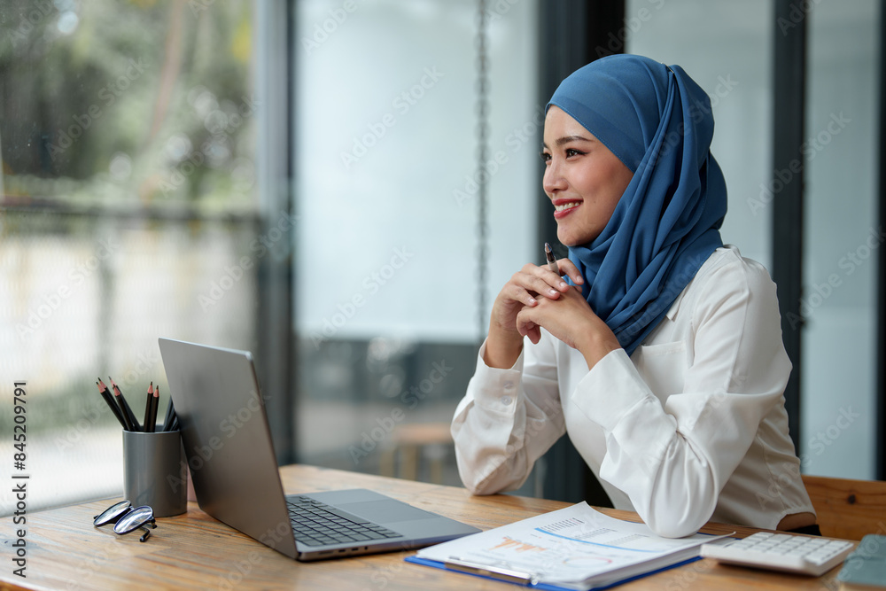 Modern office Muslim businesswoman wearing hijab sits with laptop online, doing paperwork Sitting and working on financial projects, analysis, calculations, startup business ideas, e-commerce, online.