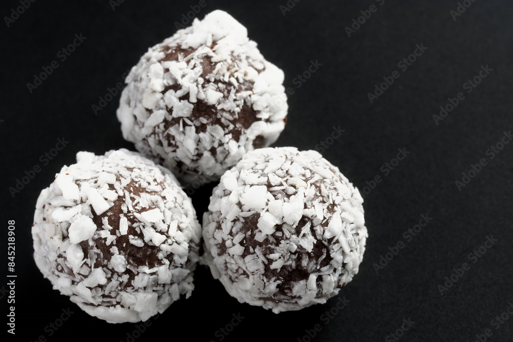 Three handmade chocolates sprinkled with coconut on a dark background. Photo. Macro. Selective focus