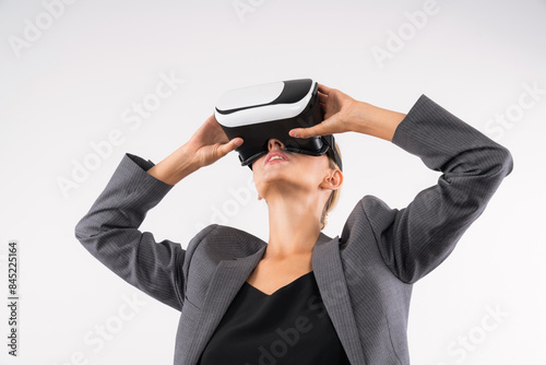 Skilled businesswoman looking at visual reality world by using VR glass while standing at background. Smart manager holding VR goggle to connect metaverse by using technology innovation. Contraption. photo