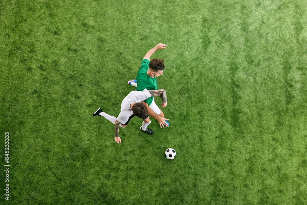 Aerial view. Dynamic photo of intense battle between two young men, soccer players for ball on green lush playground. Concept of professional sport, championship, final match, movement. Ad Aerial view. Dynamic photo of intense battle between two young men, soccer players for ball on green lush playground. Concept of professional sport, championship, final match, movement. Ad