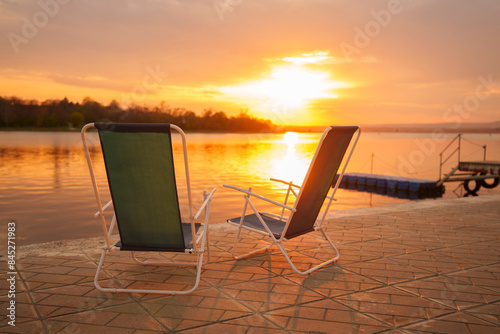 Deck chairs on pier near lake at sunset photo