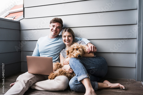 Happy couple sitting with dog in front of wall