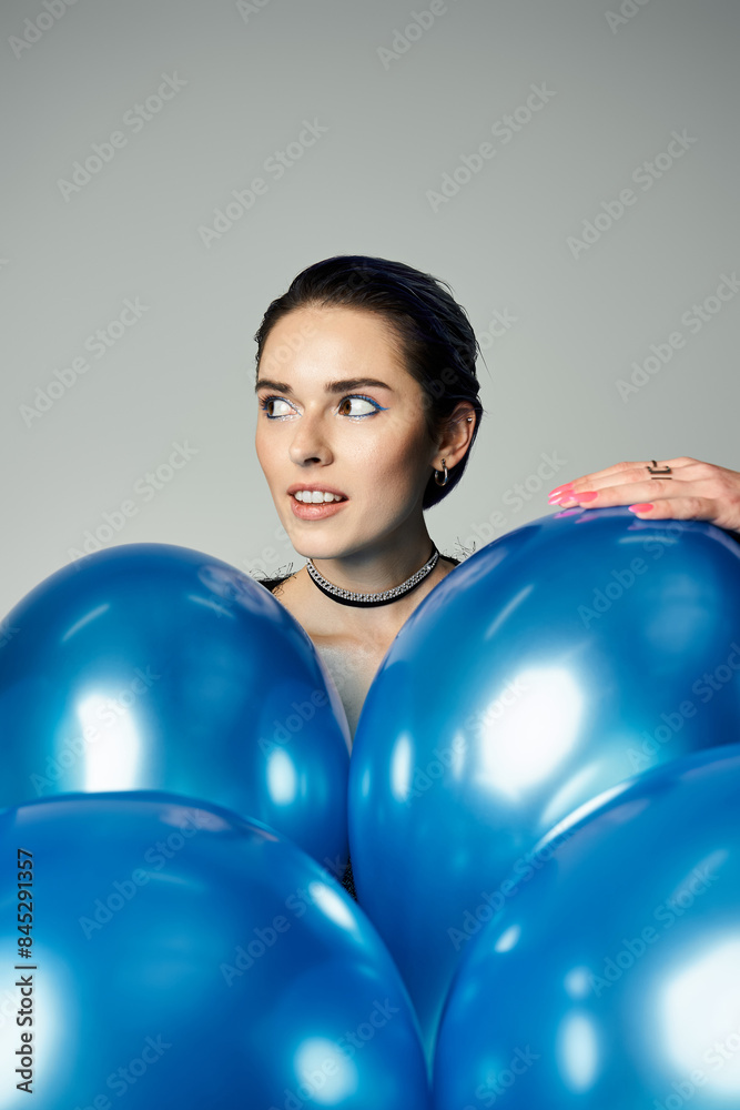 A trendy young woman with short dyed hair joyfully holds a bunch of vibrant blue balloons in a studio setting. A trendy young woman with short dyed hair joyfully holds a bunch of vibrant blue balloons in a studio setting.
