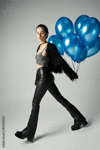 A young woman with short dyed hair poses in stylish attire, holding a bunch of blue balloons. photo