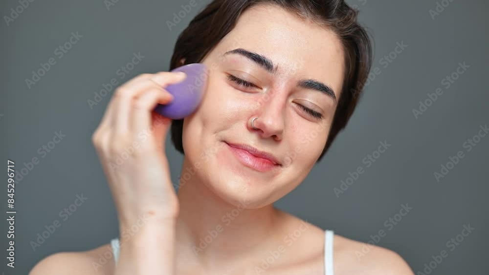 Portrait of a positive young woman doing makeup, brunette moisturizing skin with a sponge looking at the camera Portrait of a positive young woman doing makeup, brunette moisturizing skin with a sponge looking at the camera
