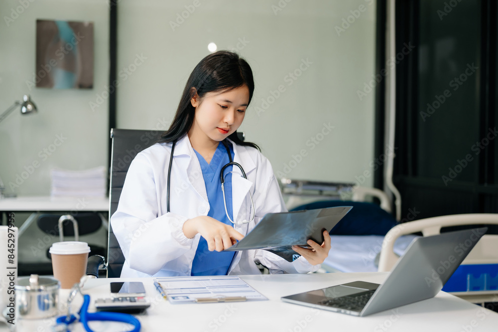 Confident young Asian female doctor in white medical uniform sit at desk working on computer. Smiling use laptop write in medical journal in clinic Confident young Asian female doctor in white medical uniform sit at desk working on computer. Smiling use laptop write in medical journal in clinic