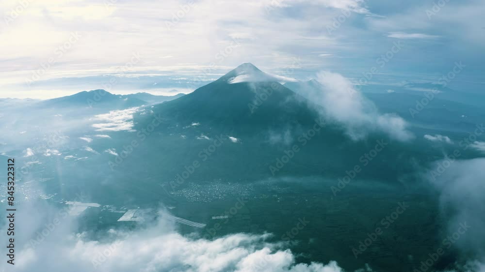 Panoramic aerial dolly to volcano with thick cloud cover breaking to reveal the cone and city Panoramic aerial dolly to volcano with thick cloud cover breaking to reveal the cone and city