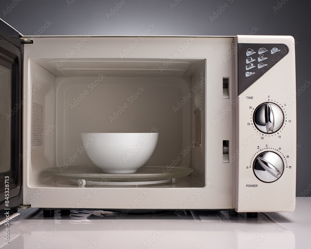 Fototapeta premium White open microwave with bowl on gray background