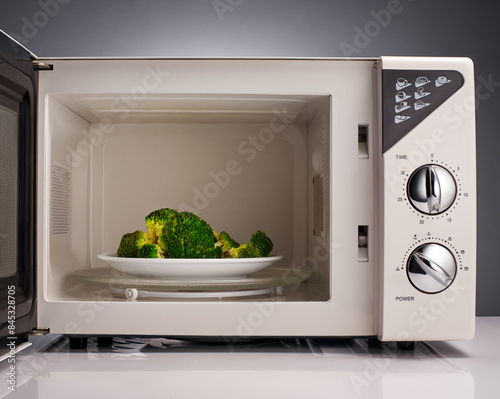 Cooked broccoli on white plate in open microwave