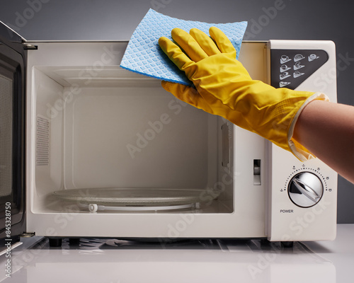 Hand in yellow glove cleaning white microwave with blue rag