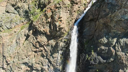 Smooth flight in the mountains above the waterfall. A powerful stream breaks down. Rainbow rays in the waterfall. Altay.