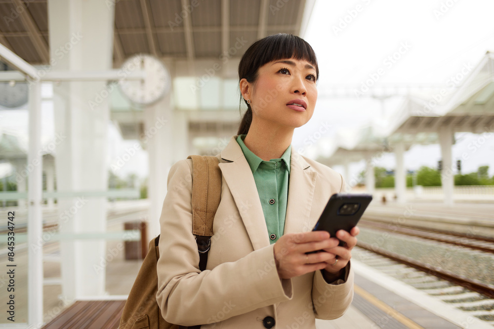 Asian businesswoman with smart phone waiting for the train at the train station Asian businesswoman with smart phone waiting for the train at the train station