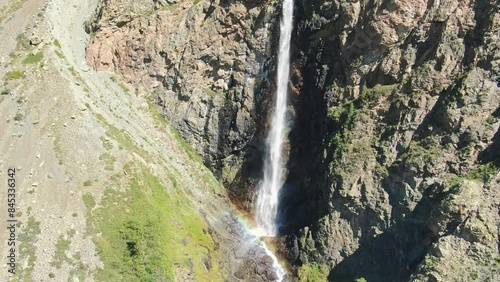 Smooth flight in the mountains above the waterfall. A powerful stream breaks down. Rainbow rays in the waterfall. Altay.