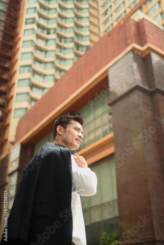 Wallpaper Mural Low angle view of millennial businessman standing in an urban street with jacket on shoulder Torontodigital.ca