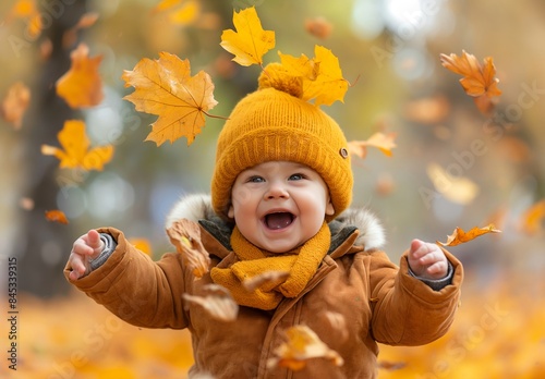 Cute happy smiling baby playing with autumn leaves on the ground, in a park, with yellow trees in the background, depicting the fall season concept.