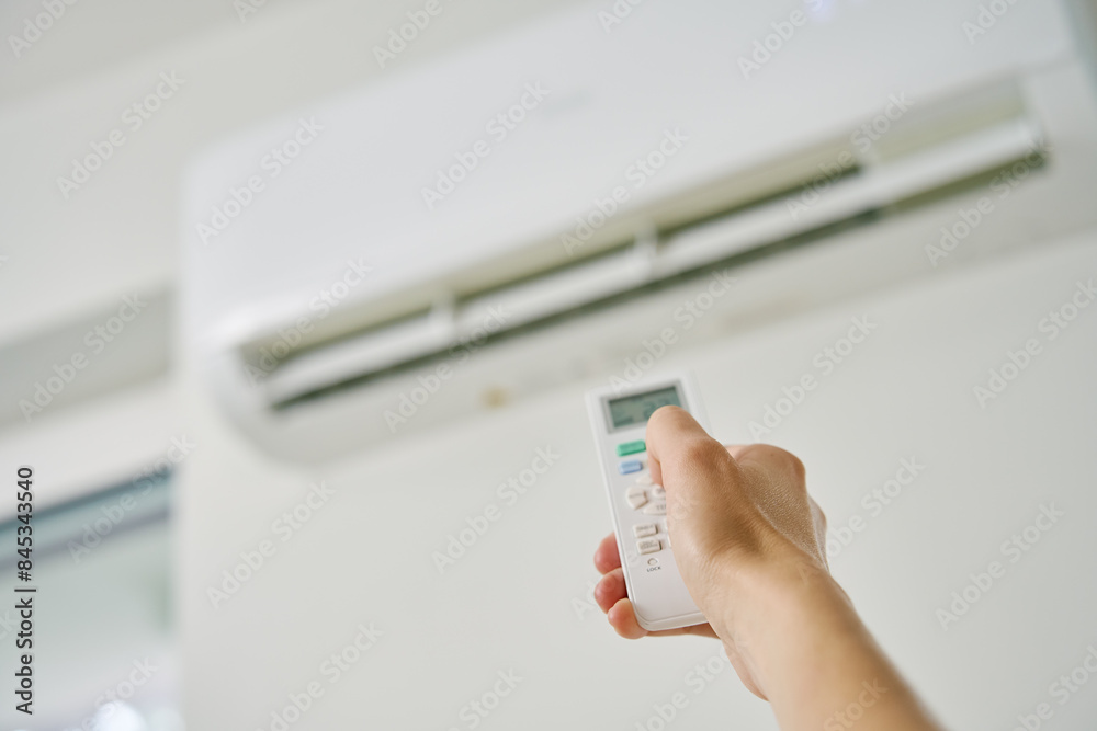 Adjusting air conditioner temperature with remote control. Hand holds remote control and setting comfortable temperature on climate system in apartment