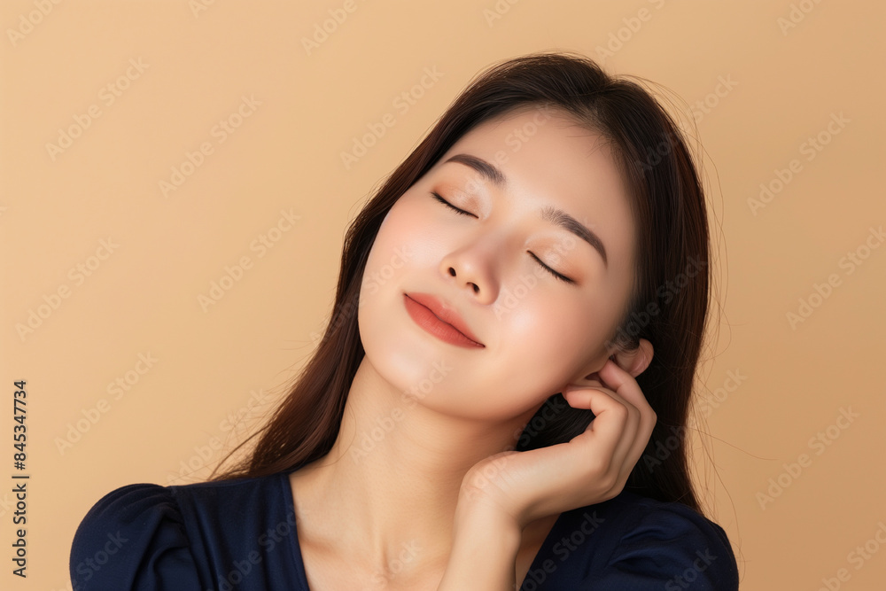 A beautiful Korean woman in her twenties with long hair, wearing navy blue and touching the side of her neck against a beige background. A beautiful Korean woman in her twenties with long hair, wearing navy blue and touching the side of her neck against a beige background.