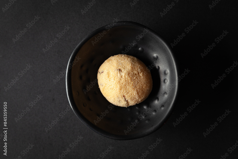 piece of coconut butter bakery cookie, placed in a black bowl on a black background. piece of coconut butter bakery cookie, placed in a black bowl on a black background.