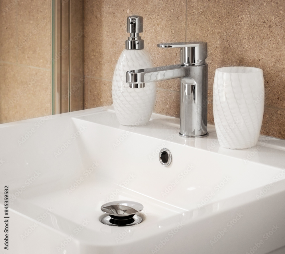 Empty white vanity counter with ceramic washbasin. A modern style faucet with tiled backsplash in a bathroom with stylish dispenser and matching beaker. Empty white vanity counter with ceramic washbasin. A modern style faucet with tiled backsplash in a bathroom with stylish dispenser and matching beaker.
