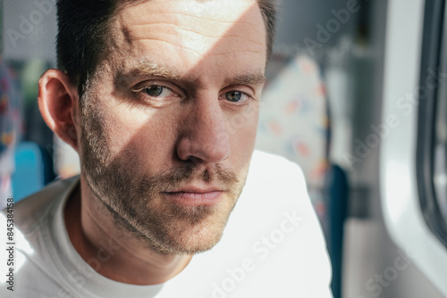 Close up picture of a serious man looking at the camera, sitting in a train 