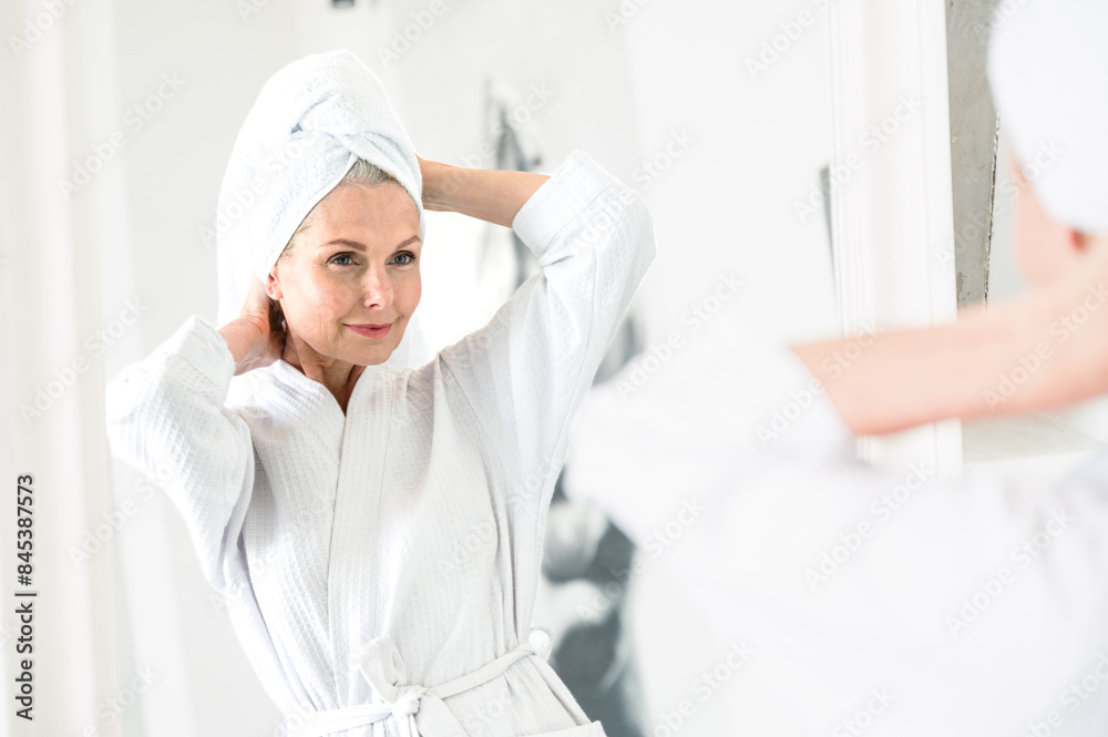 Fototapeta premium Mid age woman in bathrobe and towel relaxing after taking shower