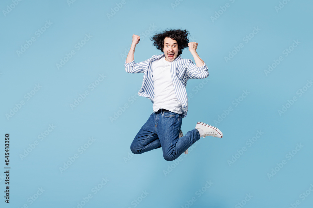 Full body young man he wear shirt white t-shirt casual clothes jump high doing winner gesture celebrate clenching fists say yes isolated on plain pastel light blue cyan background. Lifestyle concept. Full body young man he wear shirt white t-shirt casual clothes jump high doing winner gesture celebrate clenching fists say yes isolated on plain pastel light blue cyan background. Lifestyle concept.