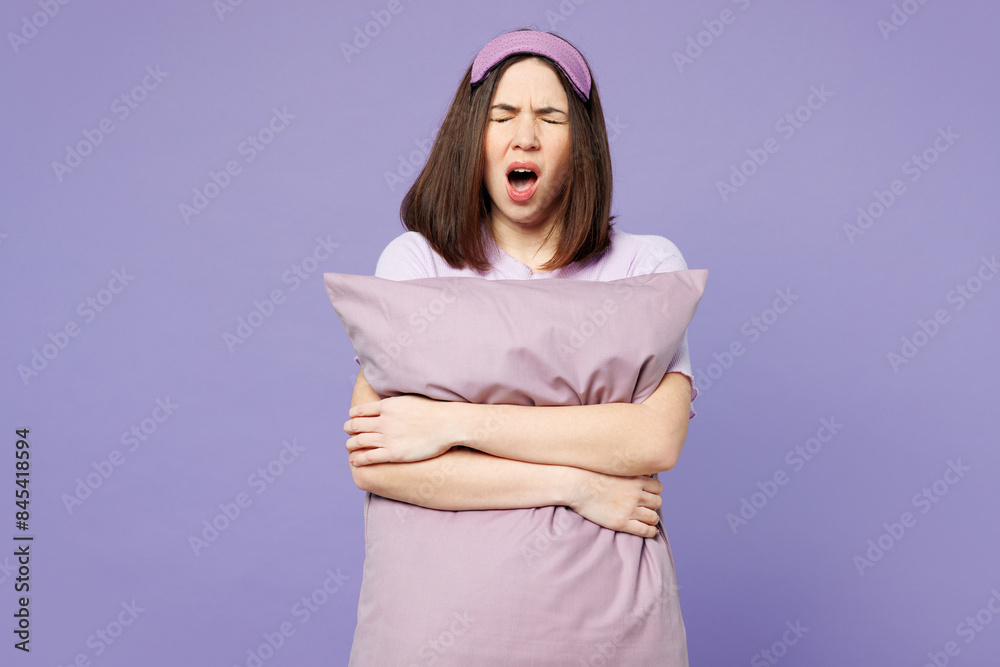 Fototapeta premium Young tired sleepy calm woman wearing pyjamas jam sleep eye mask rest relax at home hold pillow close eyes yawn isolated on plain pastel purple background studio portrait. Bad mood night nap concept.
