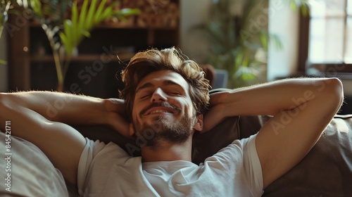 Portrait of a smiling young man relaxing at home on the couch with his eyes closed and his hands behind his head. photo